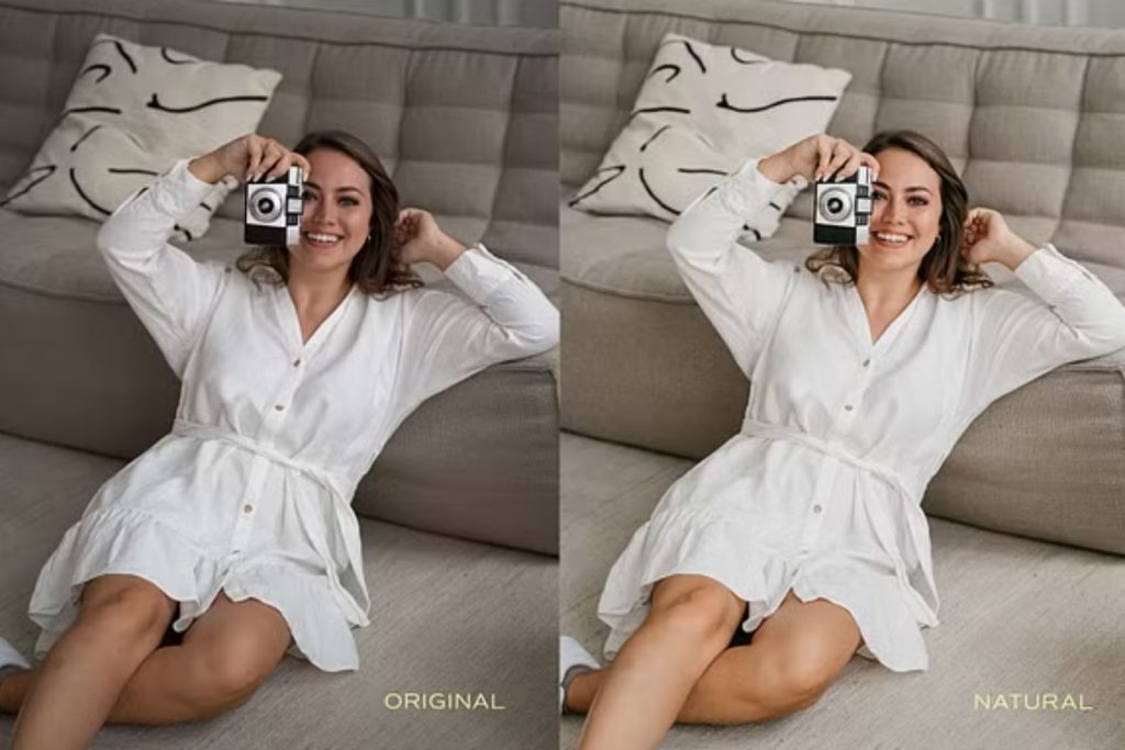 A smiling woman leaning against a couch on the floor, holding a camera in her hand.