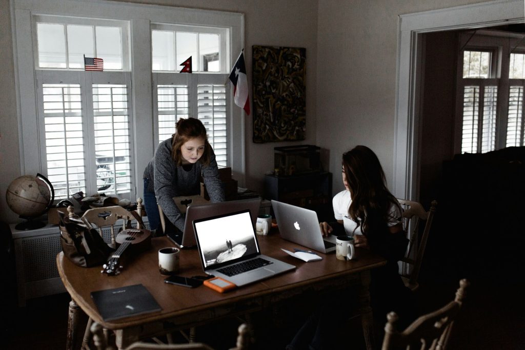 Two women working on laptops at a table.