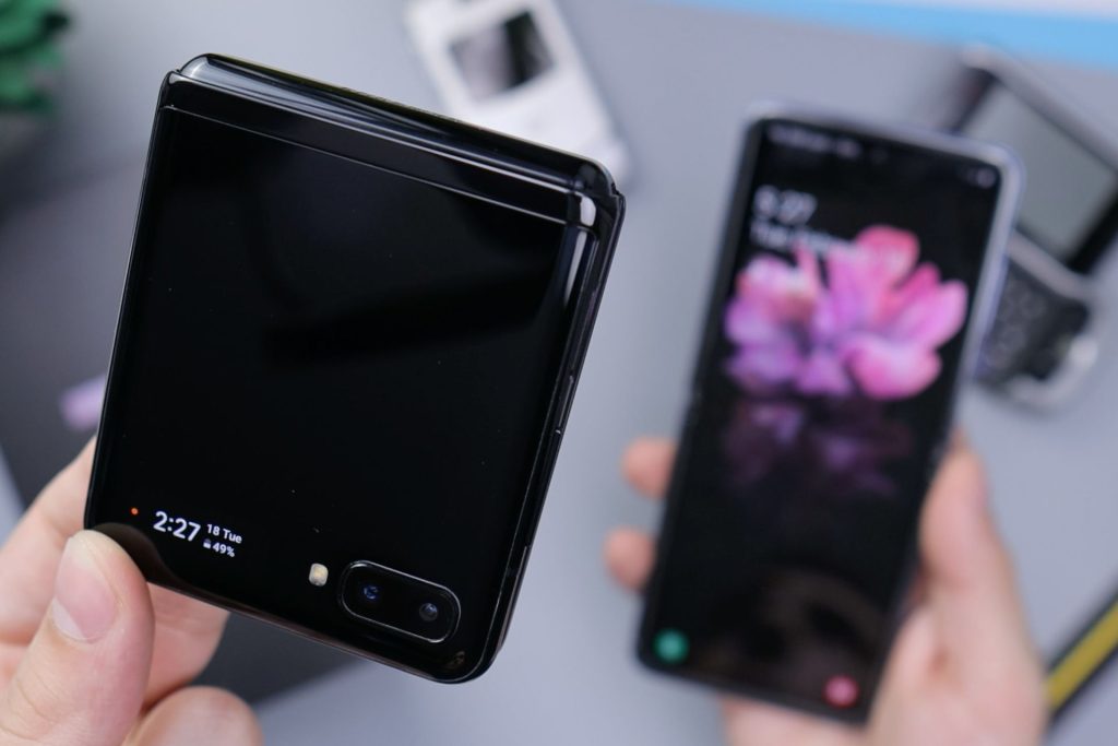 a person holding two foldable phones. One is closed and the other is open.