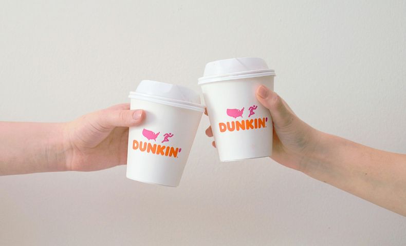 Two hands clinking white paper coffee cups printed with the new DUNKIN' wordmark in orange and pink