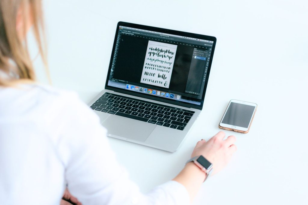 A multitasking woman efficiently manages work and communication on her laptop and phone.