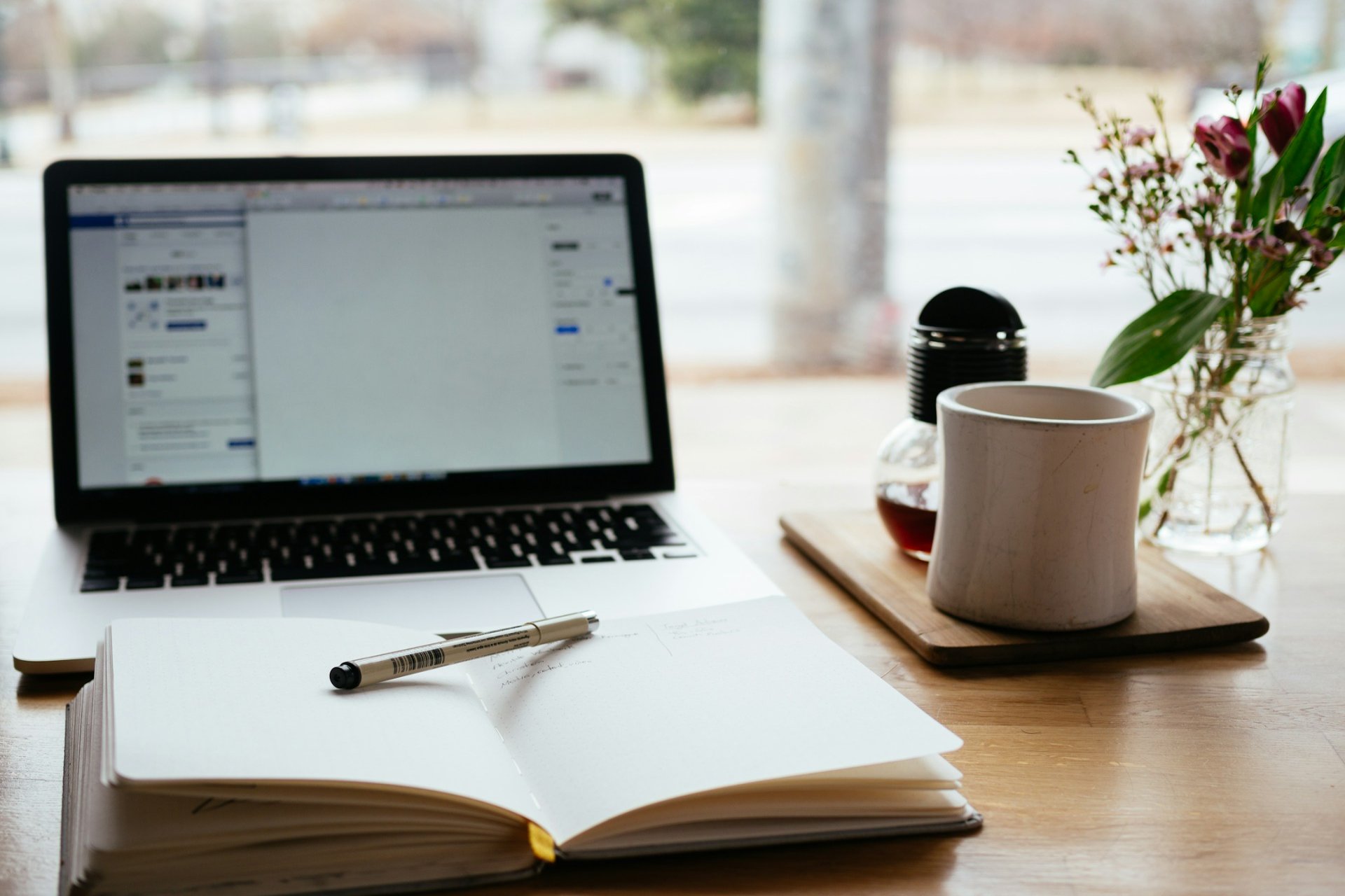 A person's workstation, with a laptop, notebook, and coffee cup on the desk.