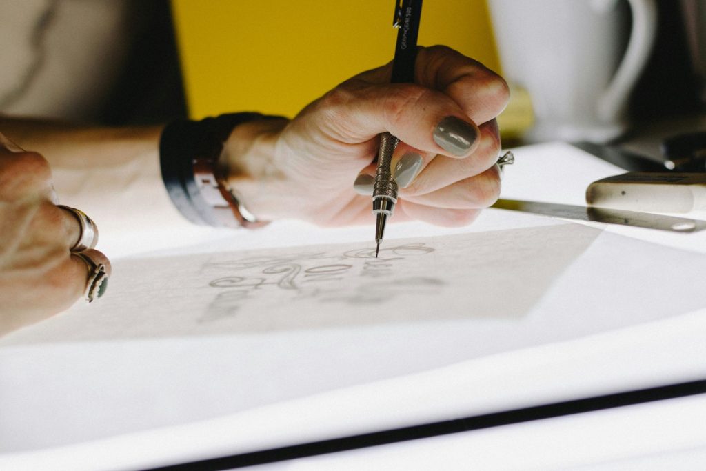 A close-up of a hand holding a mechanical pencil while sketching on a tracing light box.