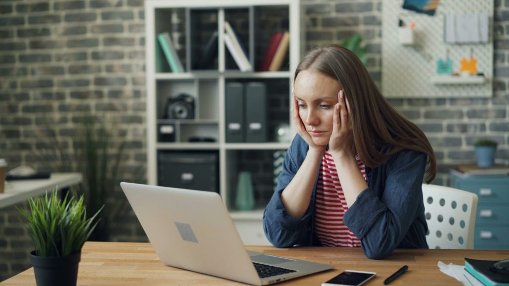A female employee hunched over a laptop showing signs of distress