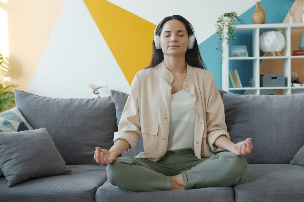 a woman meditating on her couch with headphones on