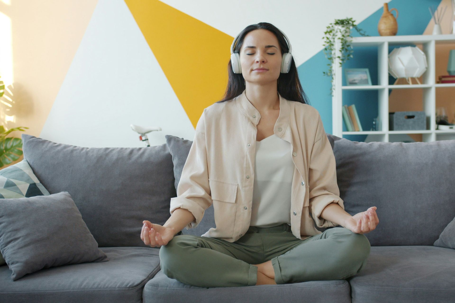 a woman meditating on her couch with headphones on