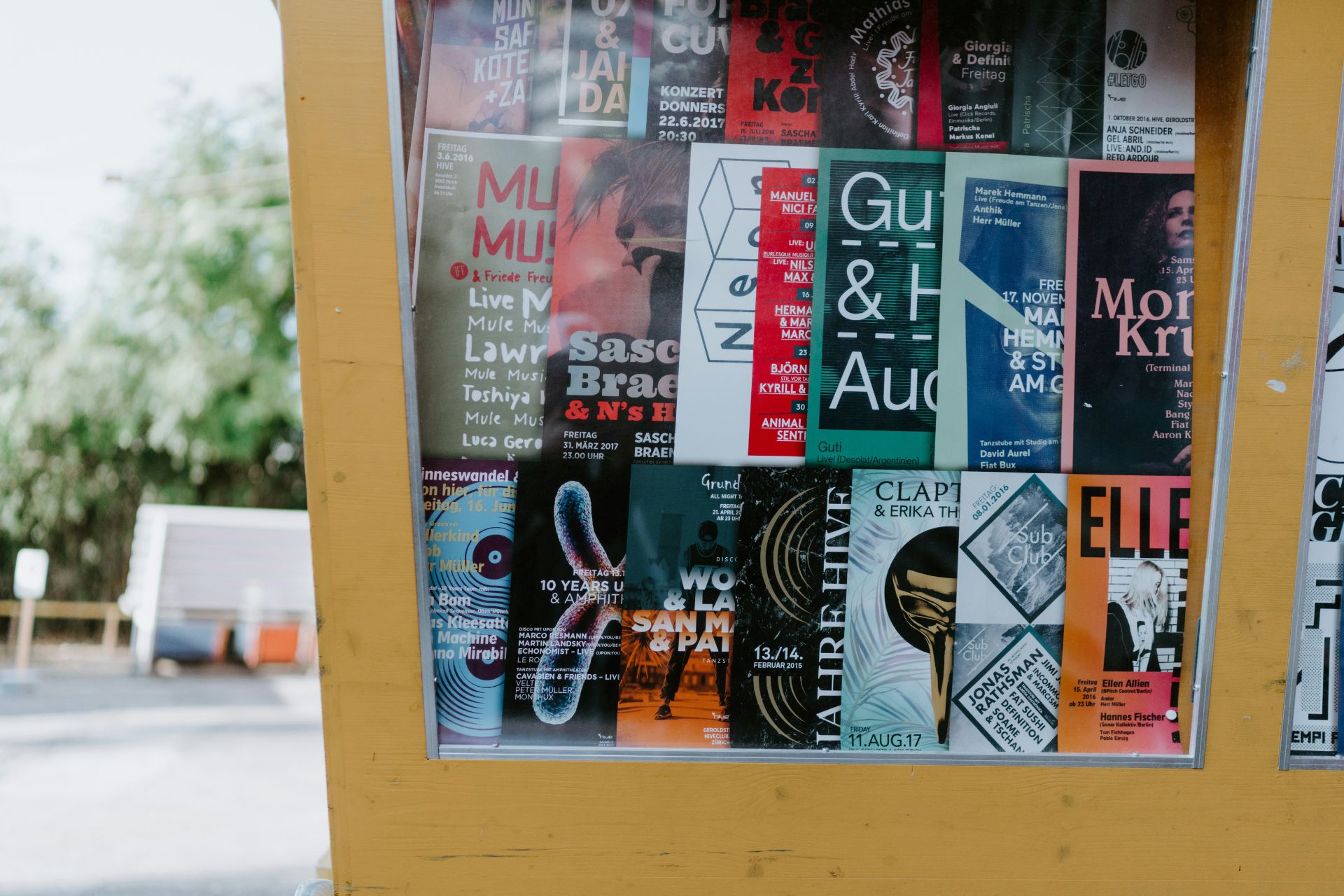 A colorful collection of event posters displayed in a yellow-framed outdoor case