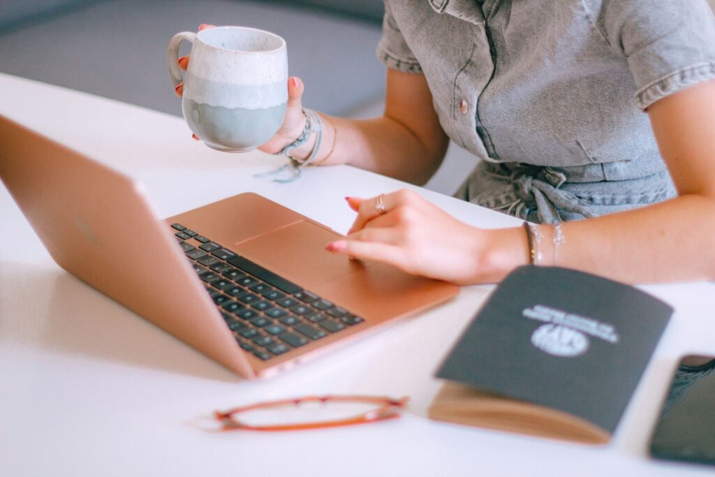 Person working on a laptop while holding a coffee mug at a desk