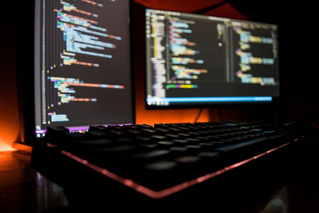 Close-up of a keyboard in front of dual monitors