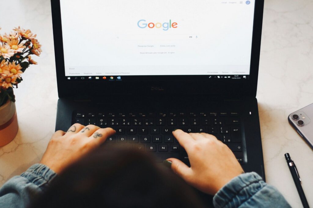 Person typing on a laptop with the Google search homepage open on the screen