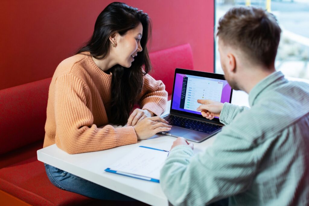 Two professionals reviewing information on a laptop while discussing a project at a table.