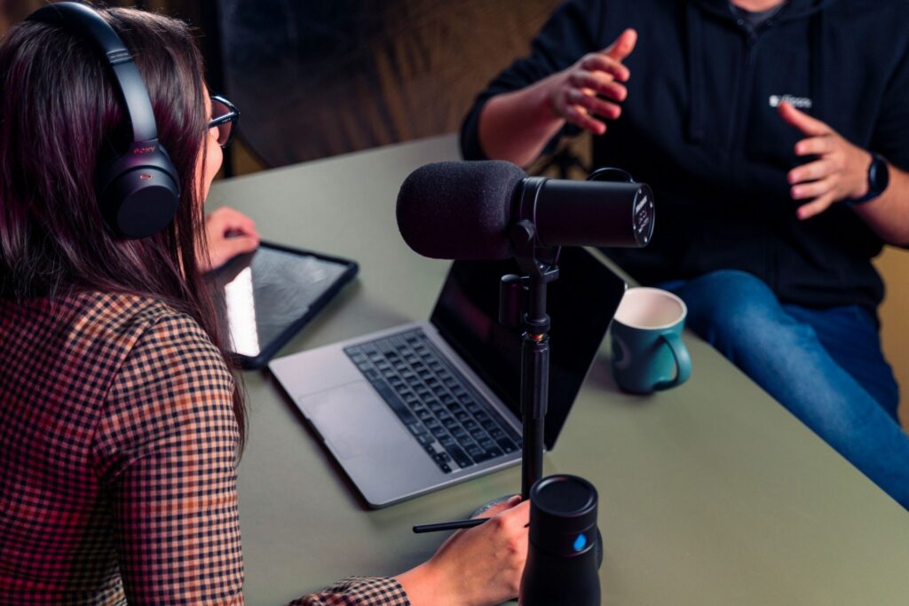 Podcast host interviewing a guest at a table with a microphone and laptop.