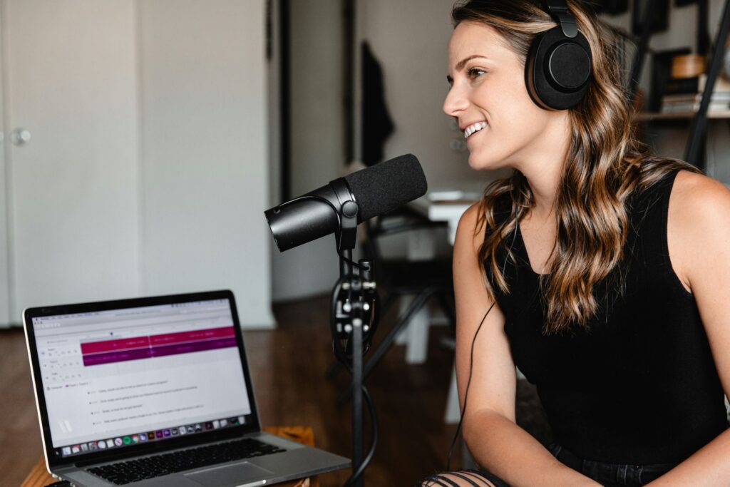 Woman wearing headphones recording a podcast with a microphone and laptop.