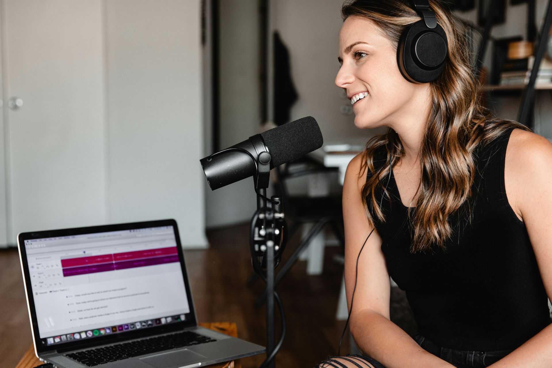 Woman wearing headphones recording a podcast with a microphone and laptop.