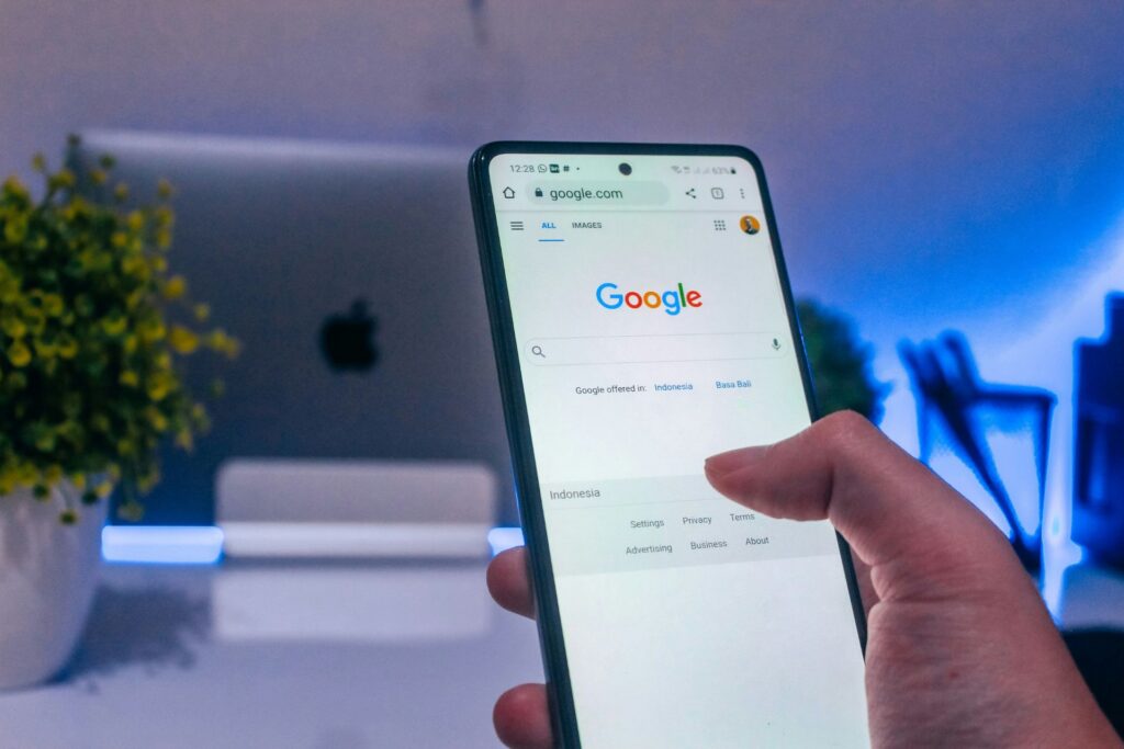 Person using Google Search on a smartphone in front of a desktop computer.