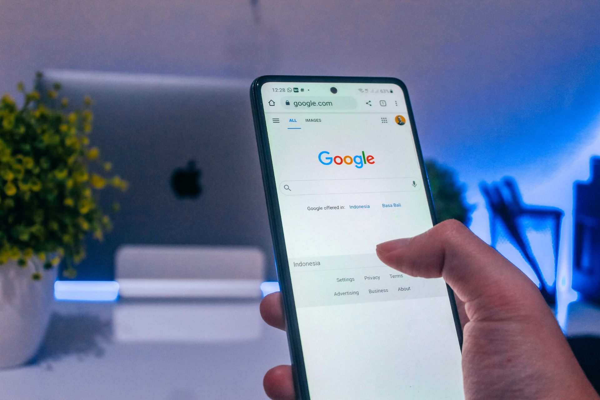 Person using Google Search on a smartphone in front of a desktop computer.