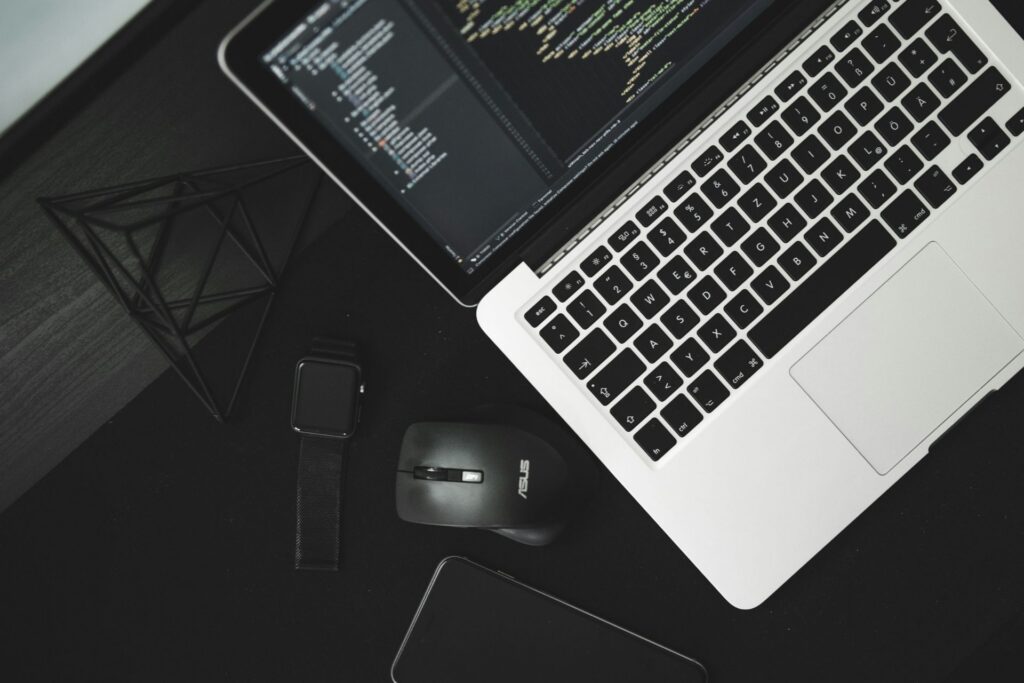 Laptop displaying code beside a smartwatch and computer mouse