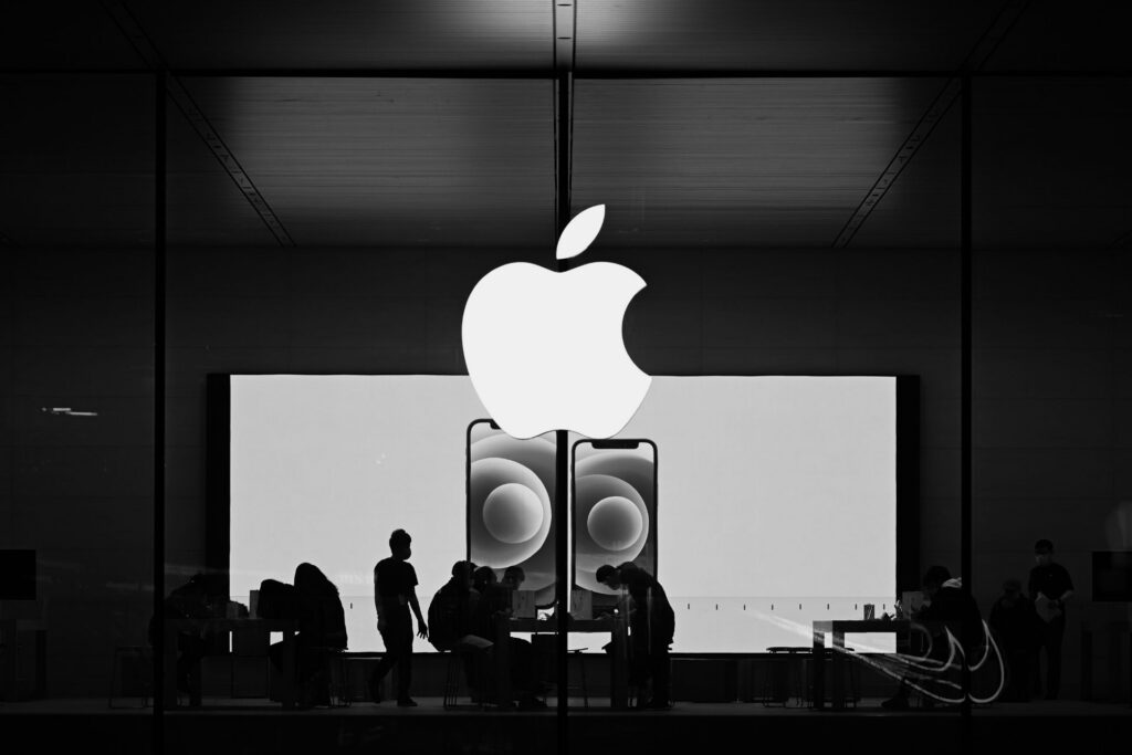 Illuminated Apple logo above an iPhone display, with silhouetted shoppers inside the store.