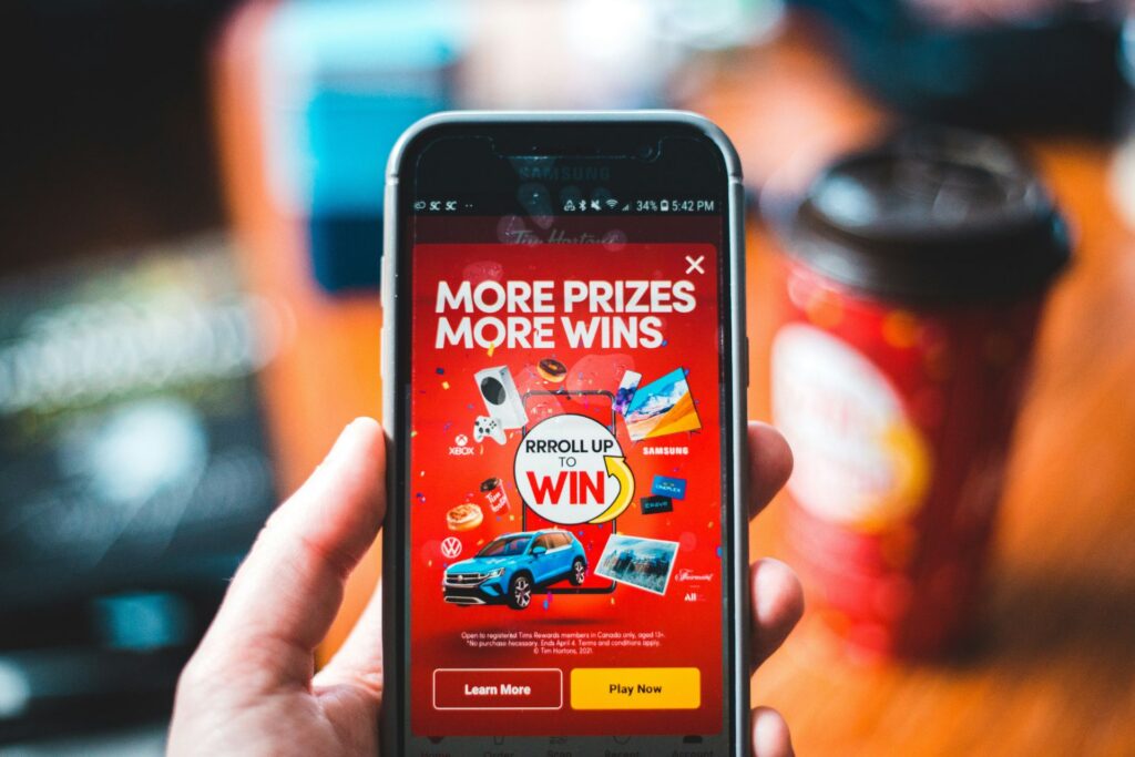 A person holds a smartphone displaying a colorful giveaway promotion with the words "More Prizes, More Wins."