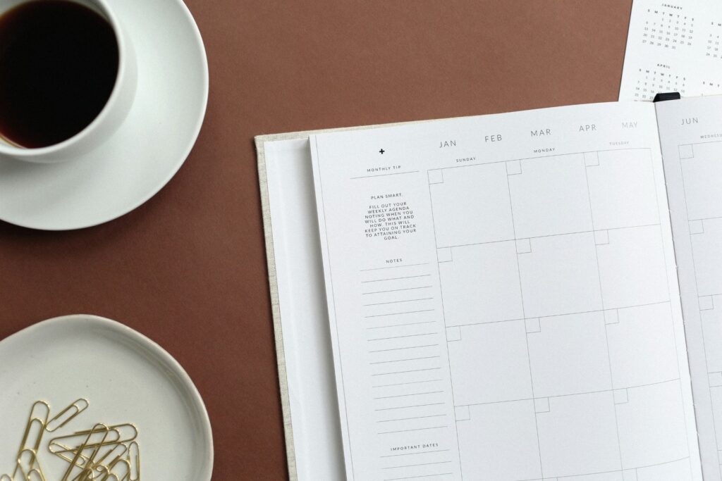 A planner sitting on a desktop next to a coffee and gold paper clips