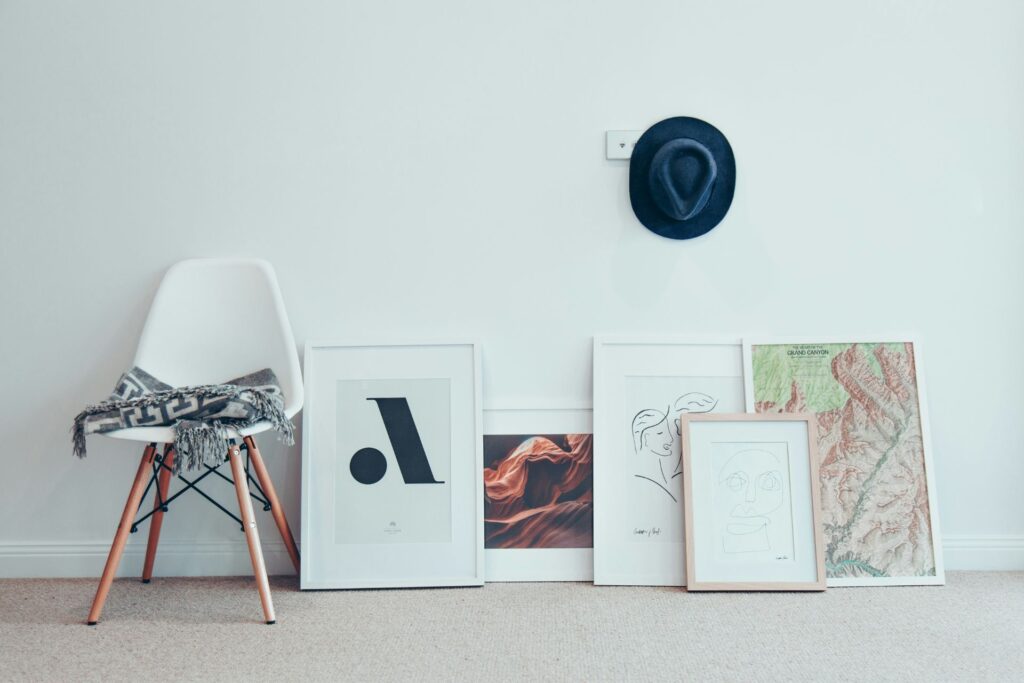 framed posters sitting against a white wall next to a chair with a throw blanket