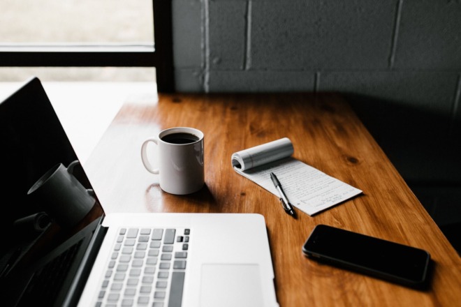 laptop standing on a table with a cup of coffee, notepad and mobile phone
