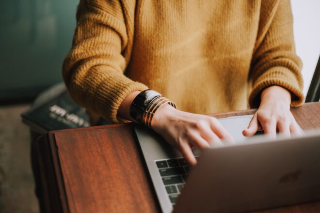 A person wearing a sweater and typing on a laptop
