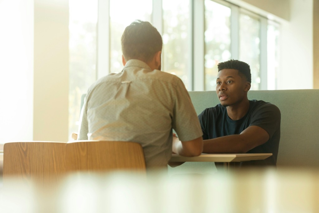 two men sitting at a table talking and building better communication skills for design work