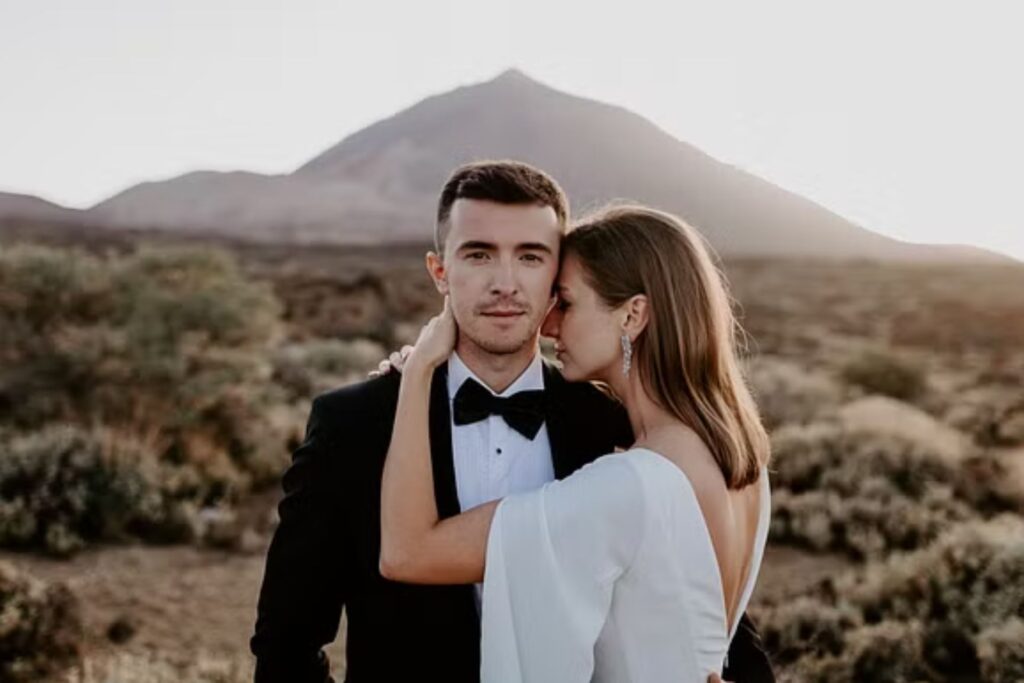 A bride and groom share a warm embrace in the desert at sunset