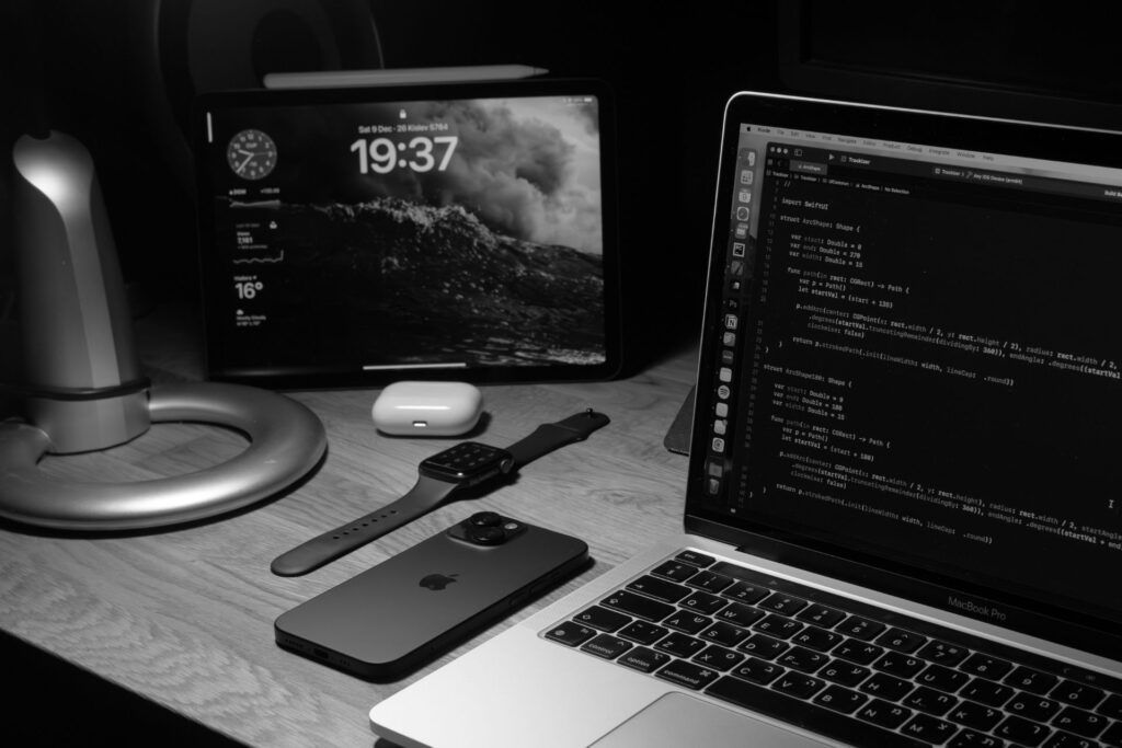 A laptop, smartphone, and various electronic devices arranged neatly on a wooden desk.