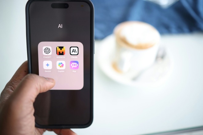 A hand holding a mobile phone displaying several AI apps.