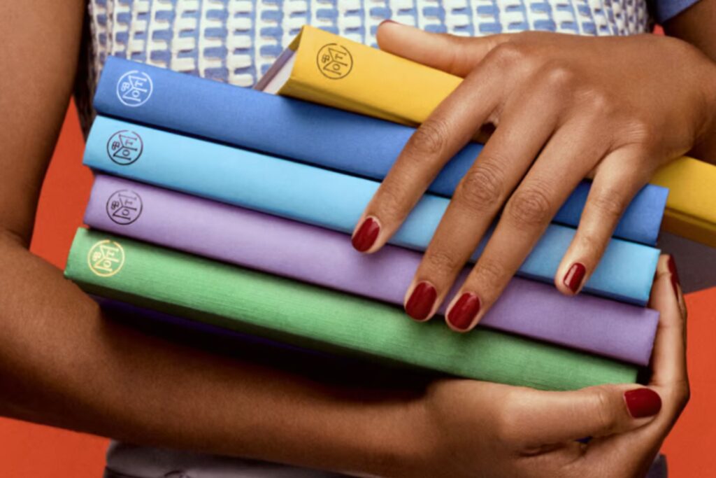 A person holding a stack of colorful hardcover books.