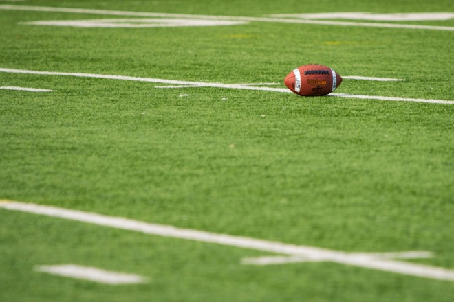 A close-up of an American football resting on a green field with white boundary lines.