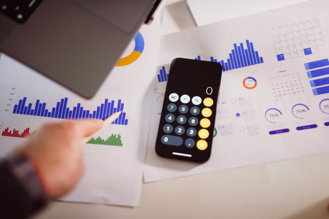 Phone calculator sits on documents showing various charts and graphs.