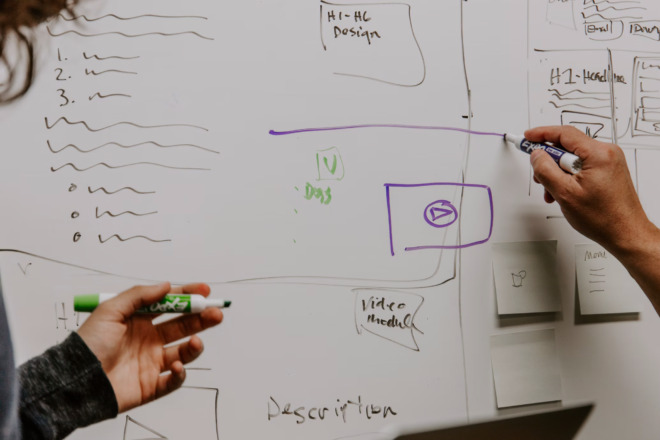 Two people brainstorm website layout and marketing strategies on a whiteboard.