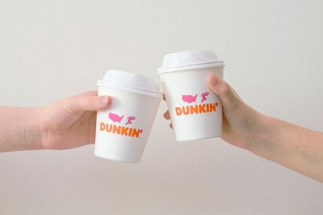 Two hands clinking white paper coffee cups printed with the new DUNKIN' wordmark in orange and pink